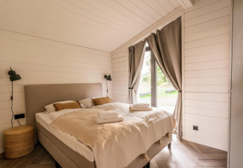 Lyst, hyggeligt soveværelse med dobbeltseng, store vinduer og gardiner på Lakehouse + hottub, Wilsumer Berge.