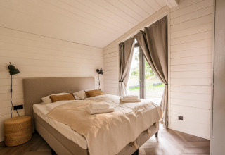 Acogedor dormitorio luminoso con cama doble, ventanales y cortinas en Lakehouse + Hottub, Wilsumer Berge, Alemania.