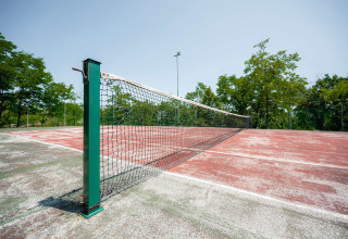 Outdoor tennis court with a worn red surface and net at Camping Centro Vacanze San Marino, Italy.