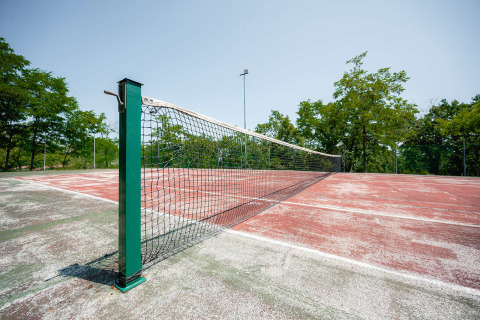 Udendørs tennisbane med slidt rød overflade og net på Camping Centro Vacanze San Marino, Italien.