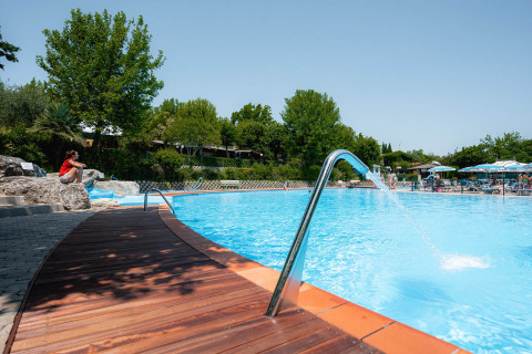 Outdoor swimming pool with wooden deck, lush trees, and guests at Camping Centro Vacanze San Marino, Italy.