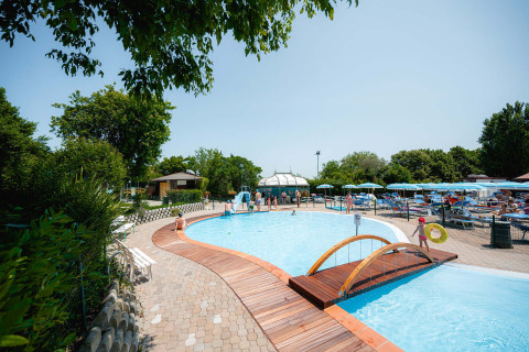 Outdoor swimming pool with wooden bridge and sun loungers at Camping Centro Vacanze San Marino, Italy, on a sunny day.