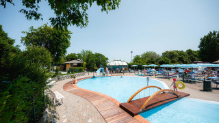 Outdoor swimming pool with wooden bridge and sun loungers at Camping Centro Vacanze San Marino, Italy, on a sunny day.