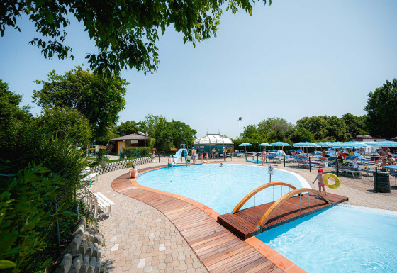 Udendørs swimmingpool med træbro og liggestole ved Camping Centro Vacanze San Marino, Italien, på en solrig dag.