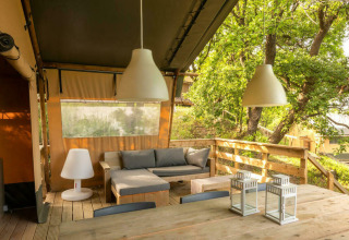 Terraza al aire libre con muebles de madera y lámparas en Camping Centro Vacanze San Marino, Italia, rodeada de árboles.