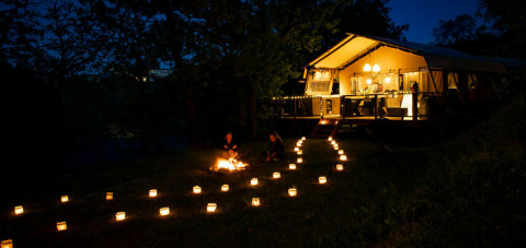 Night view of a glamping tent and lantern walkway with campfire at Camping Centro Vacanze San Marino, Italy.