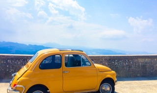 Yellow vintage car parked by a stone wall overlooking mountains near Cailungo, San Marino, Italy.