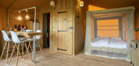 Interior view of a Desert Lodge safari tent at Camping Centro Vacanze San Marino with dining area and bed.