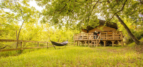 Safari tent Desert Lodge with wooden deck and hammock surrounded by lush green trees at Camping Centro Vacanze San Marino.