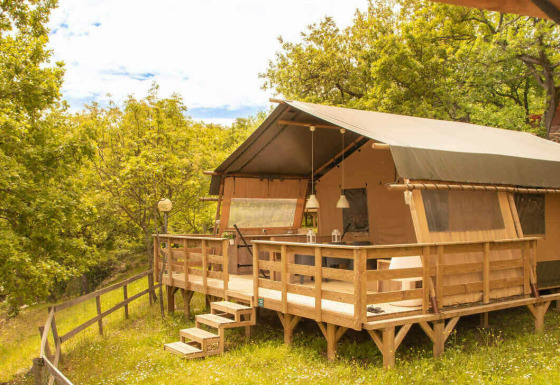 La tenda safari Desert Lodge si trova rialzata su una terrazza in legno, circondata da foresta verde.
