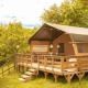 Safari-teltet Desert Lodge står hævet på trædæk i en frodig, grøn skov, med træstakitter og sollys.