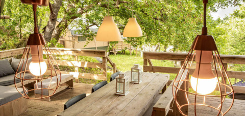 Outdoor dining area with wooden furniture and pendant lights at Desert Lodge safari tent in San Marino, Italy.