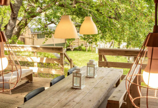 Zona pranzo esterna con tavolo in legno e lampade sospese alla tenda Desert Lodge del Camping San Marino, Italia.