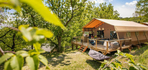 Safari tent Desert Lodge + sanitary with spacious wooden deck surrounded by trees and lush greenery outdoors.