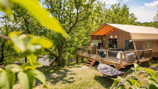 Tienda safari Desert Lodge + sanitario con terraza de madera, rodeada de árboles y naturaleza verde.