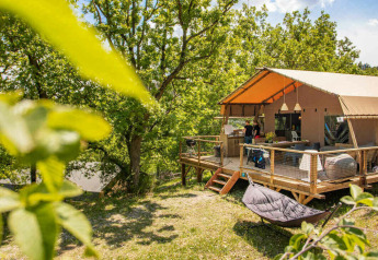 Tenda safari Desert Lodge + servizi igienici con terrazza in legno immersa nella natura e alberi verdi.