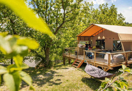 Tenda safari Desert Lodge + servizi igienici con terrazza in legno immersa nella natura e alberi verdi.