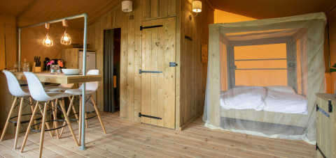 Interior of Desert Lodge safari tent with wooden furniture, dining area, and canopy bed at Camping San Marino.