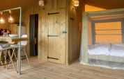 Interno della tenda safari Desert Lodge con arredi in legno, zona pranzo e letto a baldacchino a San Marino.