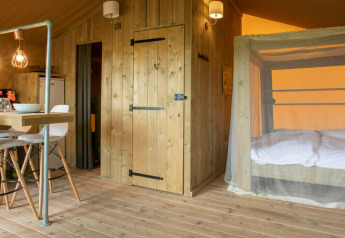 Indretning af Desert Lodge safari-telt med træmøbler, moderne spiseplads og myggenet-seng i Italien.