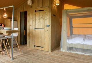 Indretning af Desert Lodge safari-telt med træmøbler, moderne spiseplads og myggenet-seng i Italien.