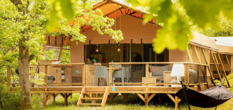 Ampia tenda safari con veranda in legno al Camping Centro Vacanze San Marino, Italia, immersa nel verde.