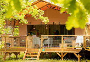 Ampia tenda safari con veranda in legno al Camping Centro Vacanze San Marino, Italia, immersa nel verde.