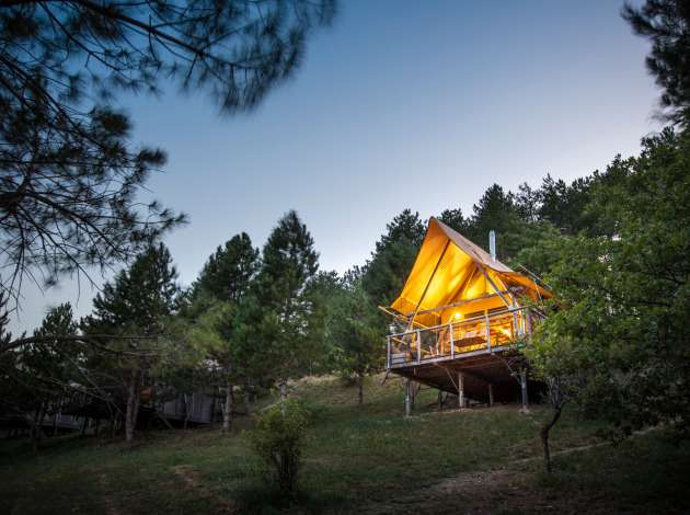 Verlichte safaritent Cahutte bij Village Huttopia Dieulefit, Frankrijk, omgeven door dennen bij schemering.