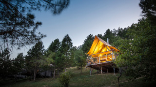 Tienda de safari iluminada Cahutte en Village Huttopia Dieulefit, Francia, rodeada de pinos al anochecer.