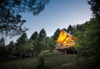 Tienda de safari iluminada Cahutte en Village Huttopia Dieulefit, Francia, rodeada de pinos al anochecer.