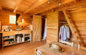 Innenraum einer gemütlichen Cahutte-Glampingunterkunft mit Küchenzeile, Garderobe und Leiter.