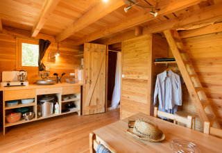 Interior of a rustic Cahutte glamping accommodation with small kitchen, dining area, and loft ladder.