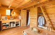 Interior de una acogedora Cahutte glamping con cocina, comedor, armario abierto y escalera al altillo.