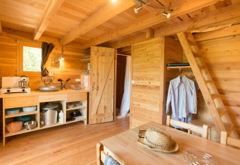 Gezellig interieur van een Cahutte glampinglocatie met open keuken, eetgedeelte en ladder naar boven.