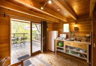Interior view of a cozy wooden cabin with small kitchen and terrace at Cahutte glamping accommodation.