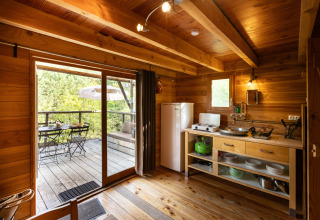 Vista interior de una acogedora cabaña de madera con pequeña cocina y terraza, en glamping Cahutte.