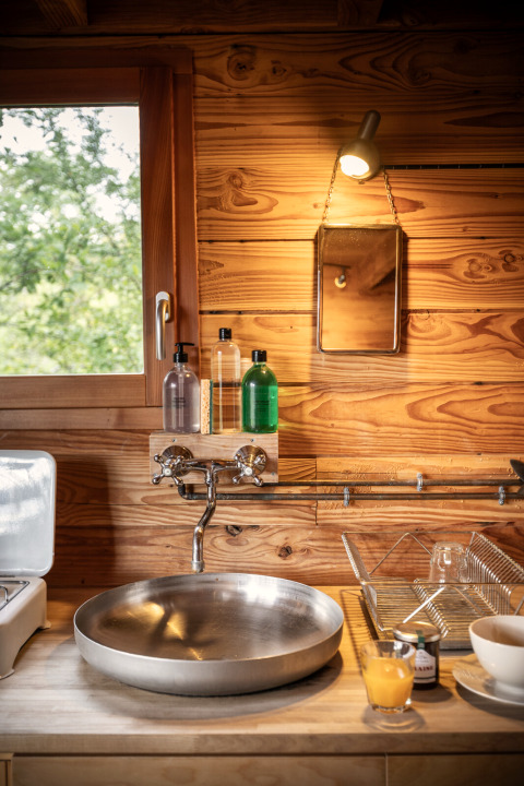 Cozy kitchen space at a Cahutte glamping lodge with wood wall, round sink, and a window to nature.