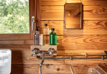 Ambiance chaleureuse dans une cuisine de glamping Cahutte, avec mur en bois, évier rond et fenêtre.