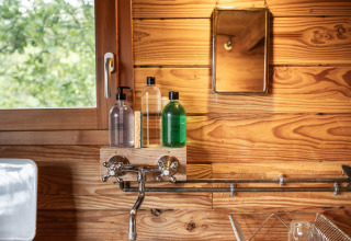 Knusse keukenruimte in een Cahutte glamping verblijf met houten wand, ronde lavabo en raam.
