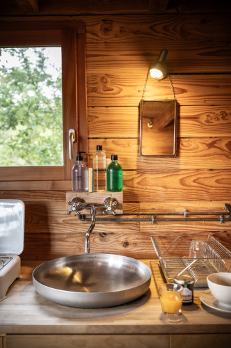 Acogedora cocina en un alojamiento glamping Cahutte con pared de madera, lavamanos redondo y ventana.