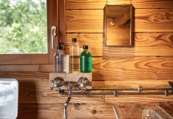 Acogedora cocina en un alojamiento glamping Cahutte con pared de madera, lavamanos redondo y ventana.