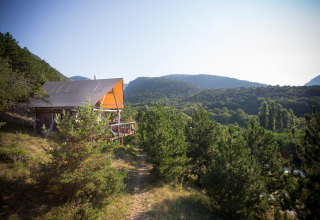 Una tienda Cahutte de safari en Village Huttopia Dieulefit, Francia, rodeada de pinos y colinas verdes.