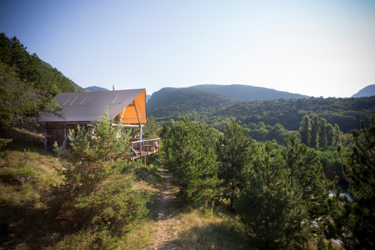 Una tienda Cahutte de safari en Village Huttopia Dieulefit, Francia, rodeada de pinos y colinas verdes.