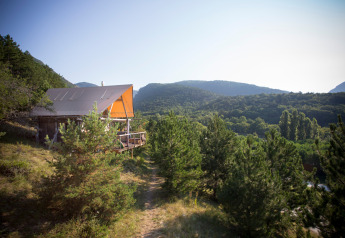 Una tienda Cahutte de safari en Village Huttopia Dieulefit, Francia, rodeada de pinos y colinas verdes.