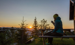 Persona disfruta de una bebida caliente en un banco al amanecer cerca de Sachsenburg, Carintia, Austria.