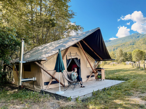 Kvinde slapper af foran et safari Trappeur-telt ved Huttopia Vallouise, Frankrig, omgivet af natur.