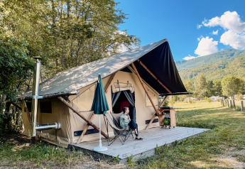 Woman relaxing outside a safari Trappeur tent at Huttopia Vallouise, France, with scenic mountain views.