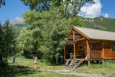 Twee kinderen spelen buiten aan een houten chalet in het groen bij Chalet Montana in Huttopia Vallouise, Frankrijk.