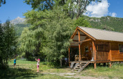 Twee kinderen spelen buiten aan een houten chalet in het groen bij Chalet Montana in Huttopia Vallouise, Frankrijk.