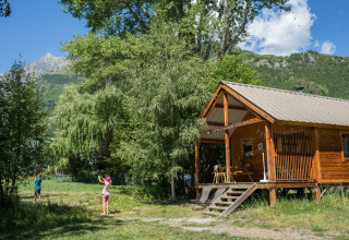 Dos niños juegan fuera de una cabaña de madera rodeada de naturaleza en Chalet Montana en Huttopia Vallouise, Francia.